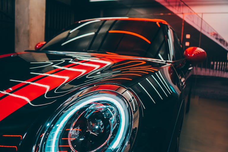 A luxury sports car in a modern setting with vibrant red and neon lights reflecting on the surface.