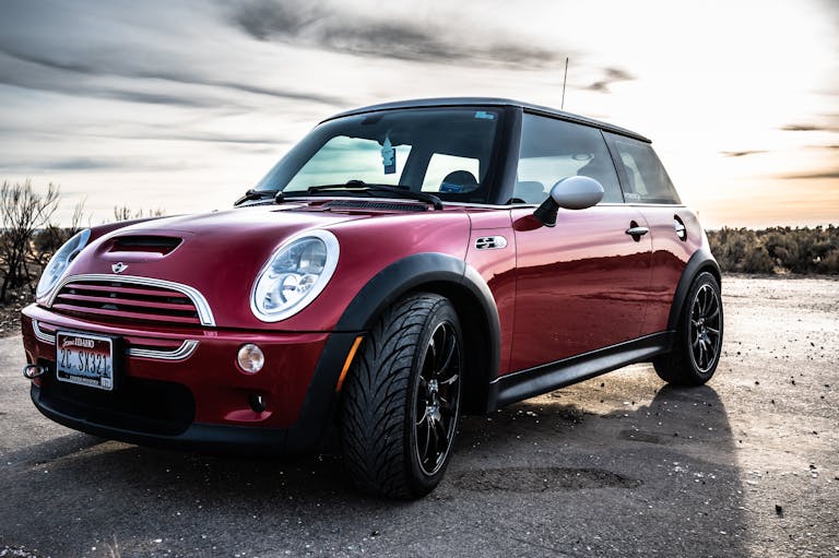 A sleek red Mini Cooper car parked on an open road with a scenic backdrop.