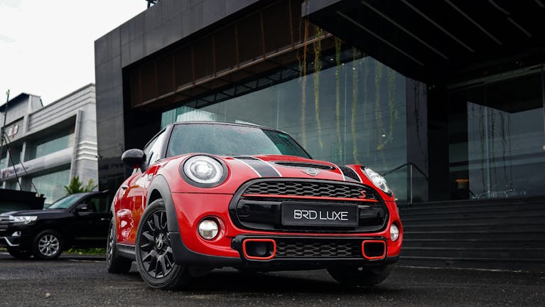 Low angle shot of a red Mini Cooper parked in front of a contemporary glass building.