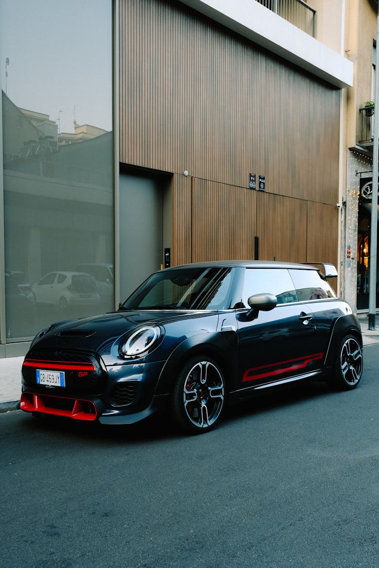 Shiny black Mini Cooper with red accents parked in city setting, showcasing luxury and style.